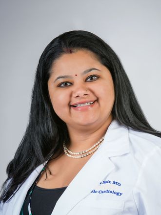 Woman in white coat, pearls, smiling, likely a doctor or healthcare professional.