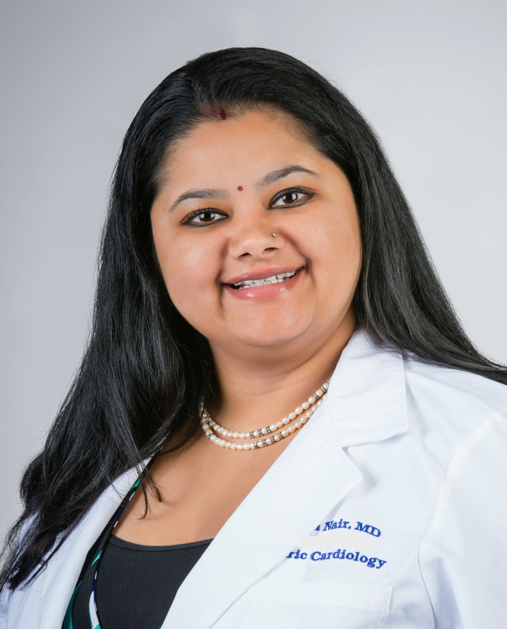 Woman in white coat, pearls, smiling, likely a doctor or healthcare professional.