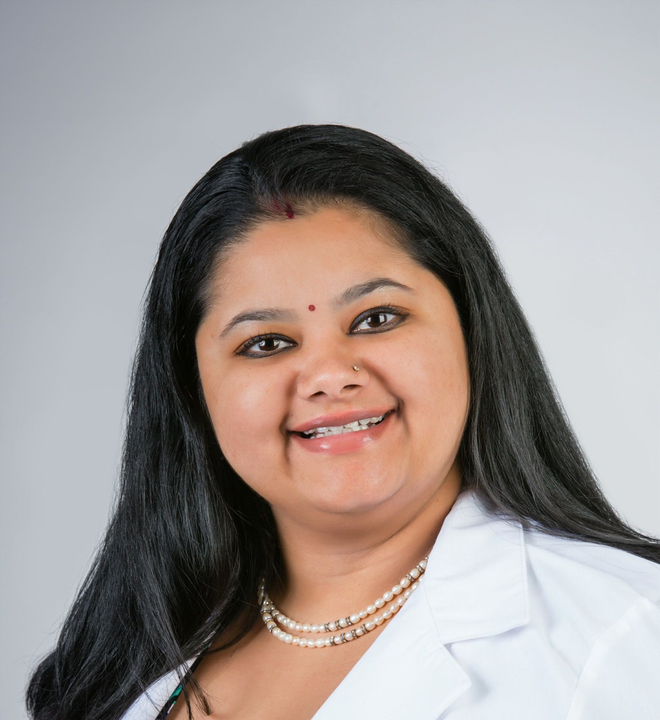 Portrait of a smiling woman in a white lab coat against a light gray background