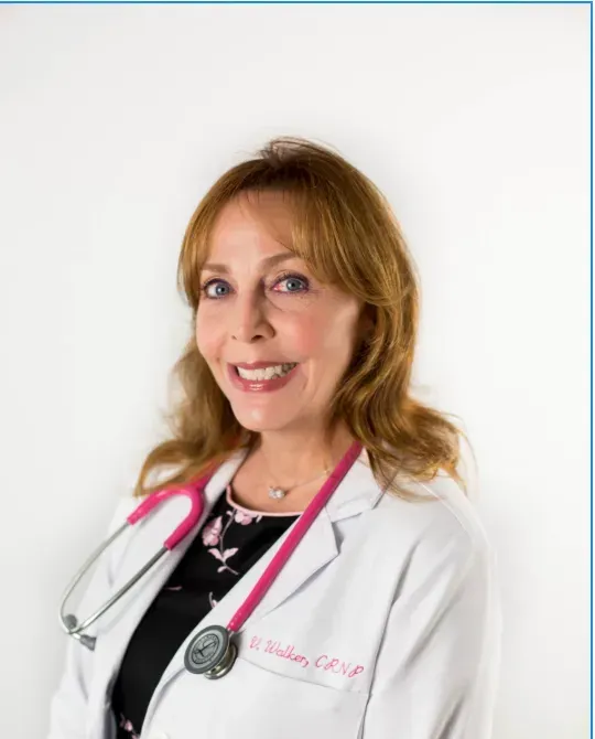 Woman with auburn hair in a white lab coat and pink stethoscope; smiling.