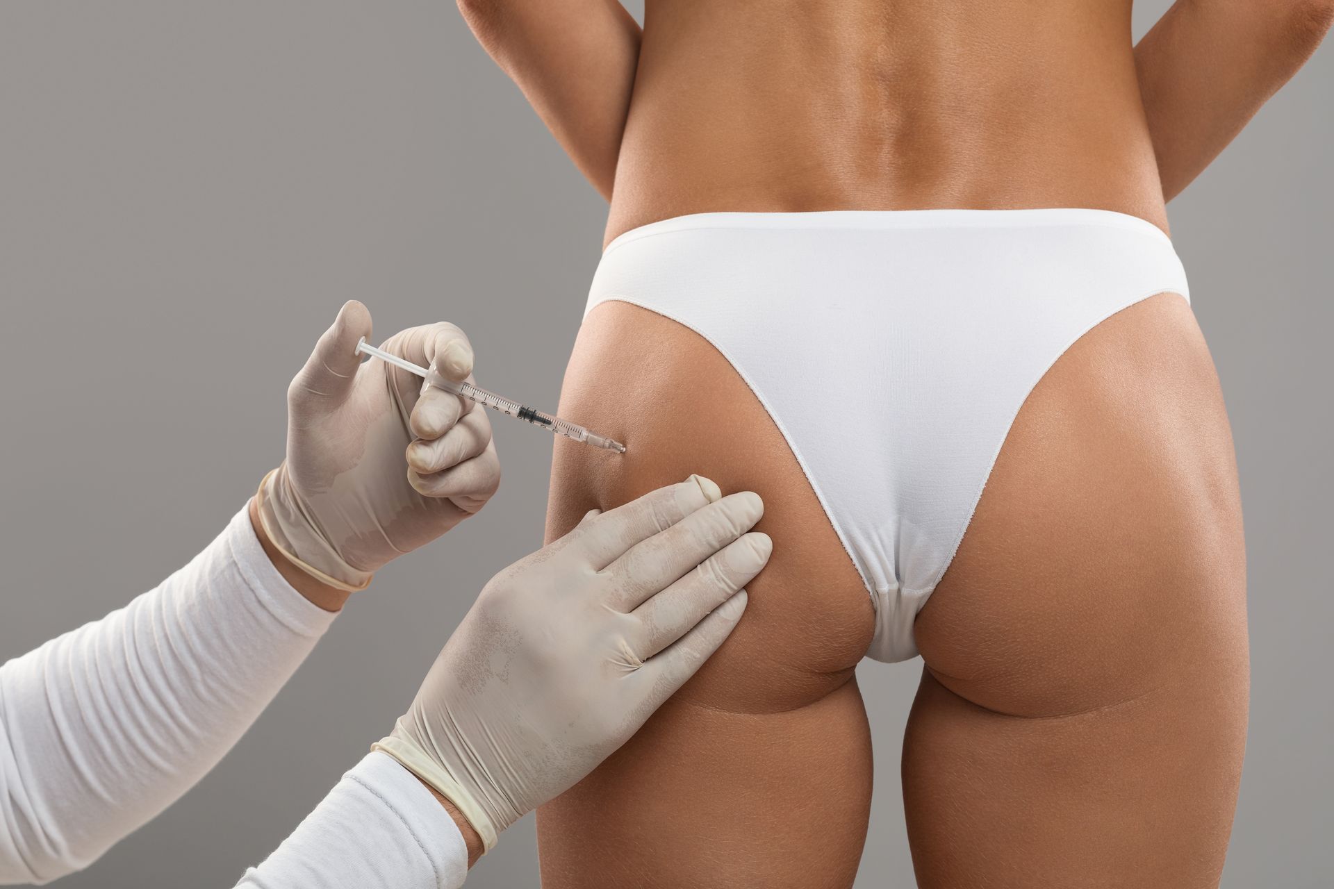 Person receiving an injection in their buttocks, with gloved hands and syringe.
