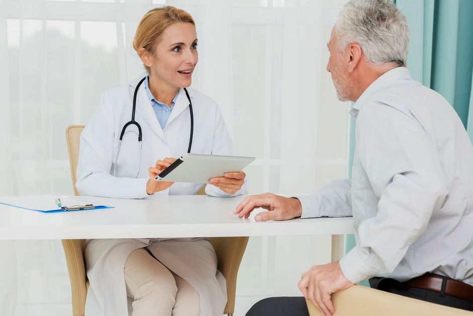 A doctor is sitting at a table talking to an older man.