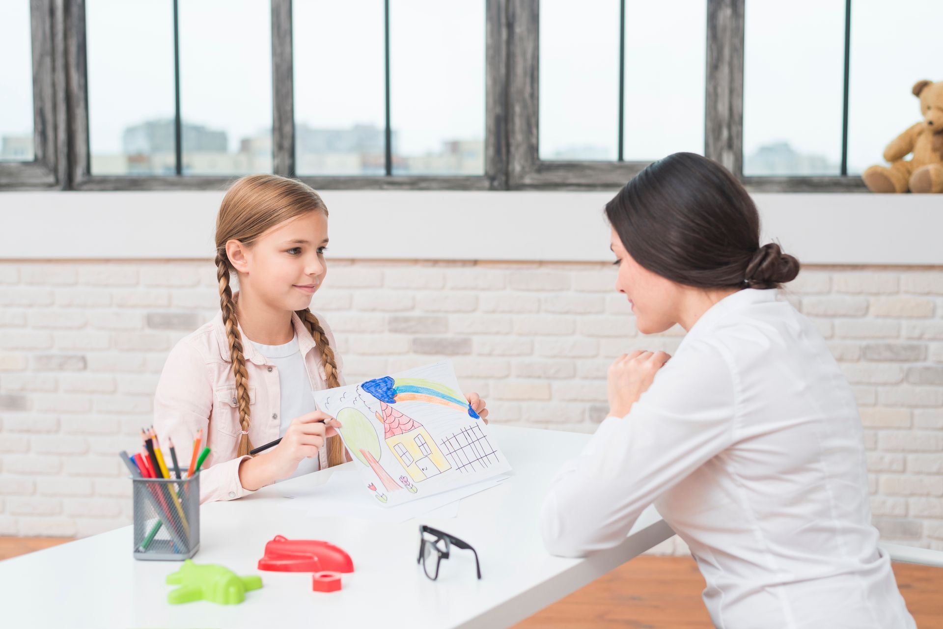 A woman is sitting at a table talking to a little girl.