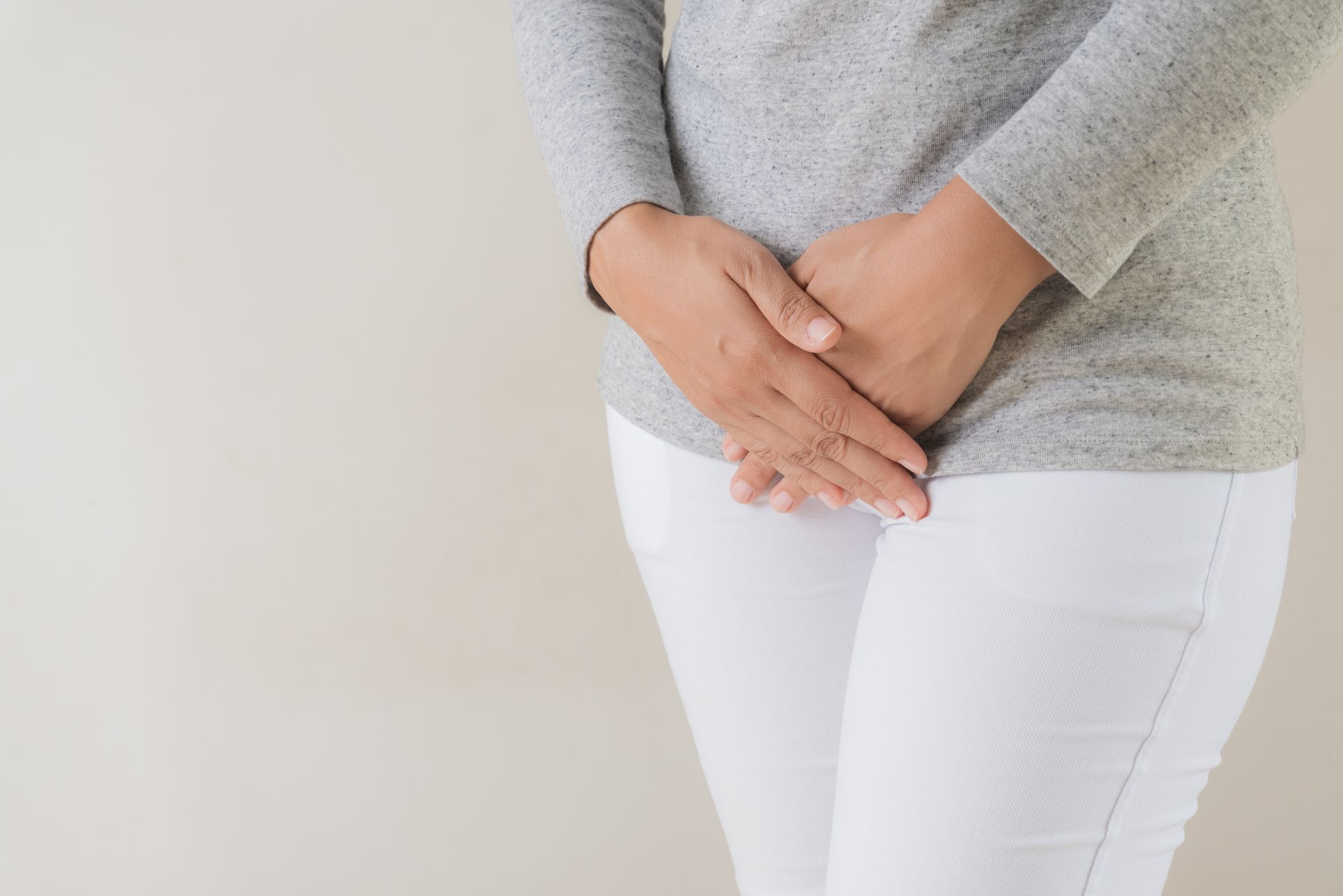 A woman is holding her hands on her lower abdomen.