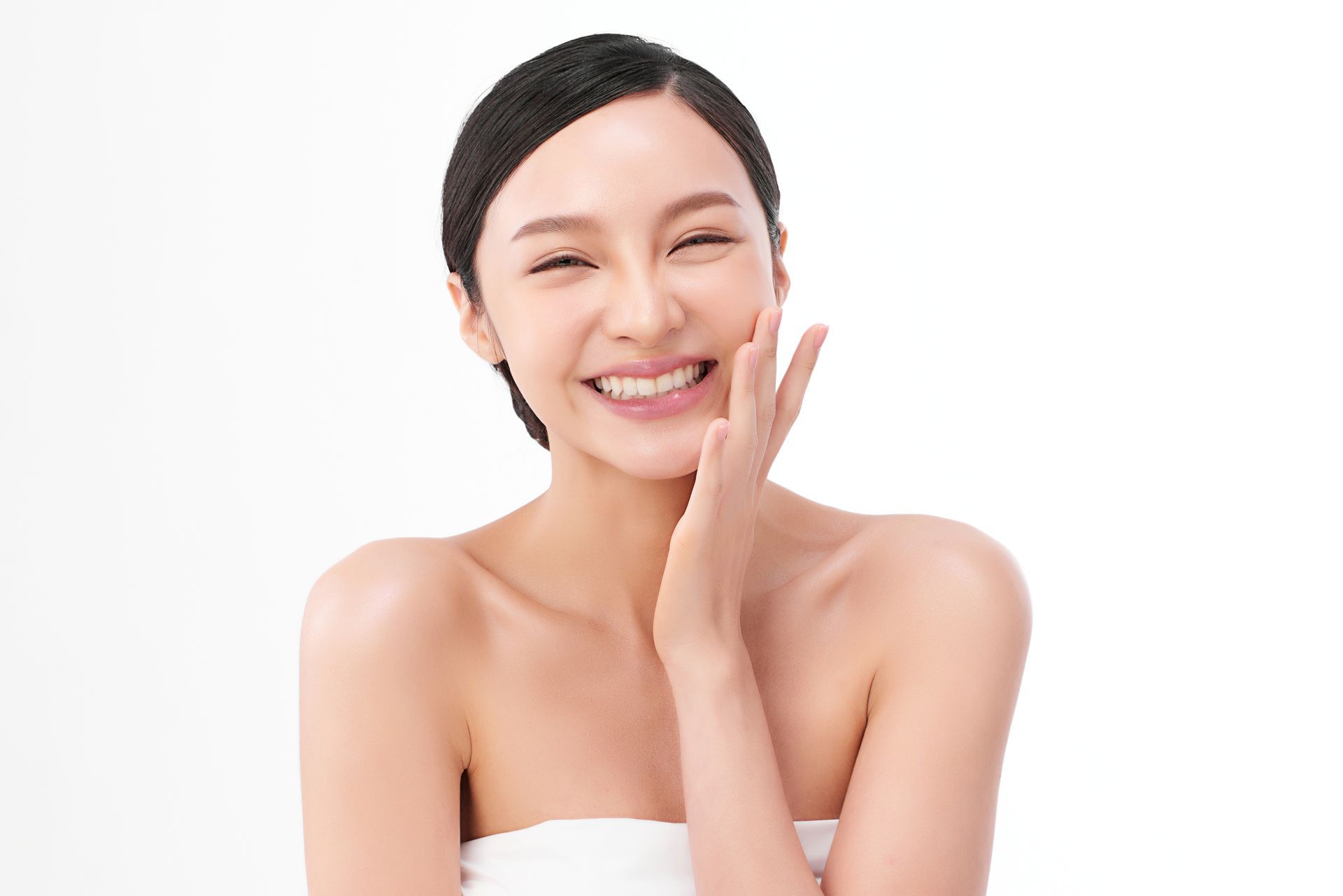 A woman is smiling and touching her face with her hand.