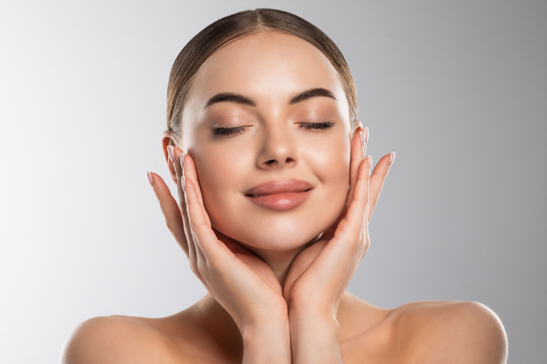 A woman is touching her face with her hands and smiling.