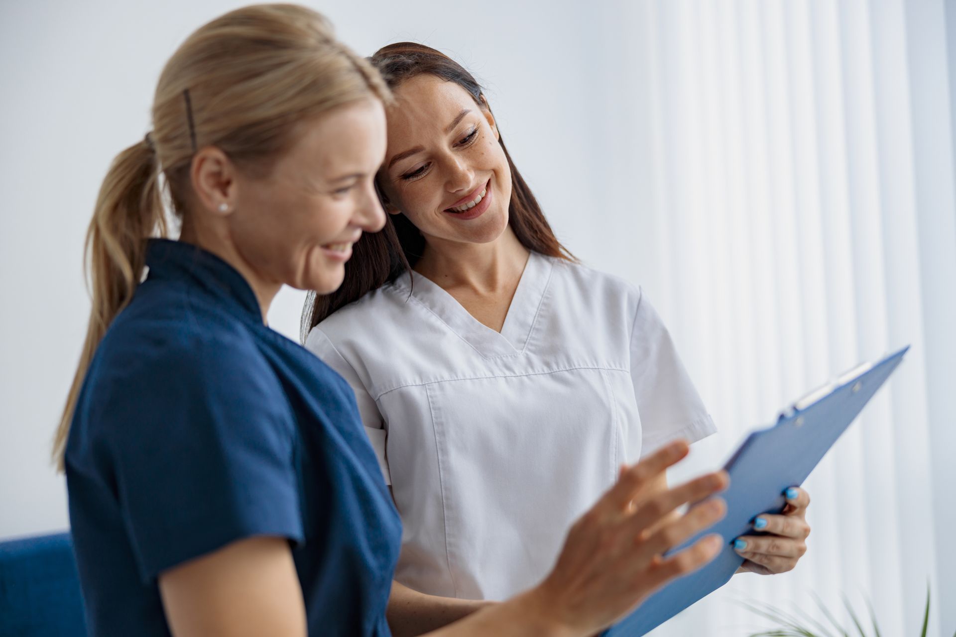 Two healthcare workers review a clipboard and smile in a bright clinical setting