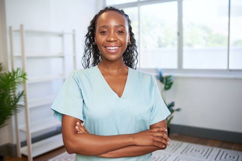 Smiling person in a light blue top stands with arms crossed in a bright room