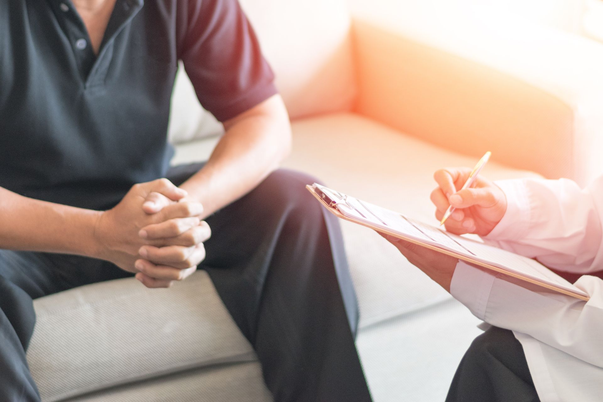 Person in dark shirt talking with a counselor taking notes on a clipboard in a bright office