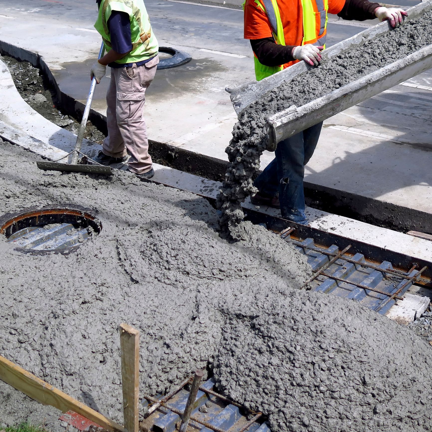 Workers pour concrete for a construction of a section of a pavement road.