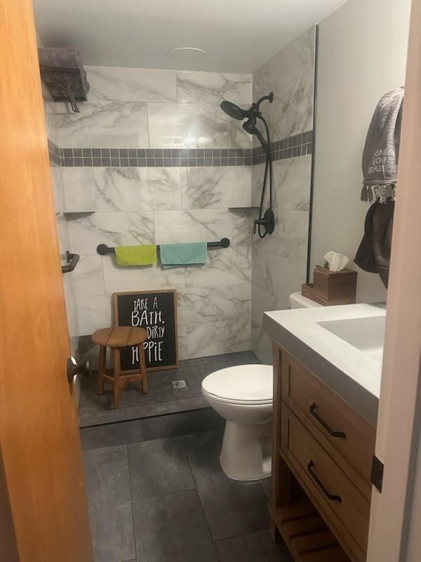 Bathroom with marble tiled shower, vanity, toilet, and wooden stool.
