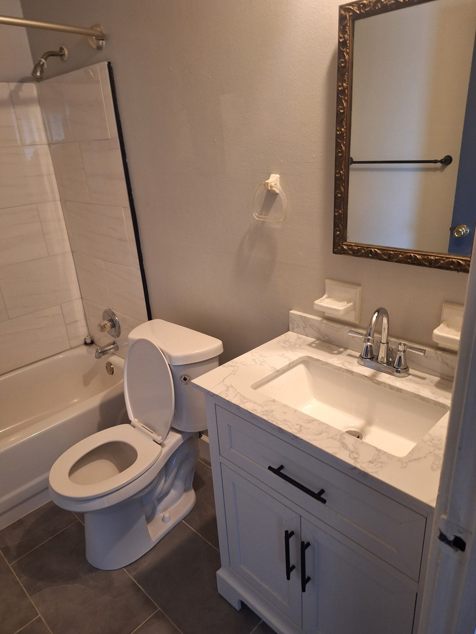 Bathroom with white toilet, vanity, and tub, and gray tile floor. Mirror above the sink.