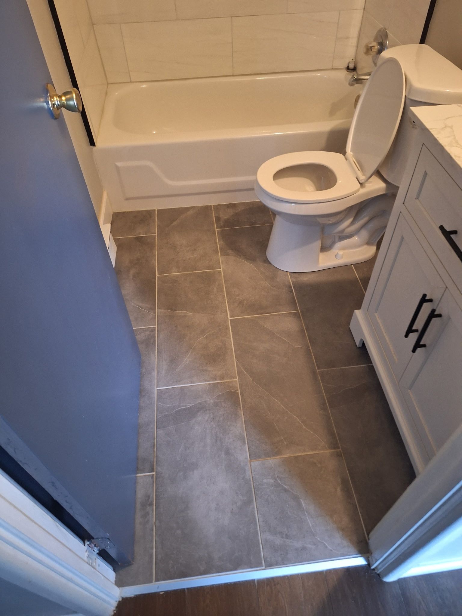 Bathroom with a toilet, tub, vanity, and gray tiled floor.