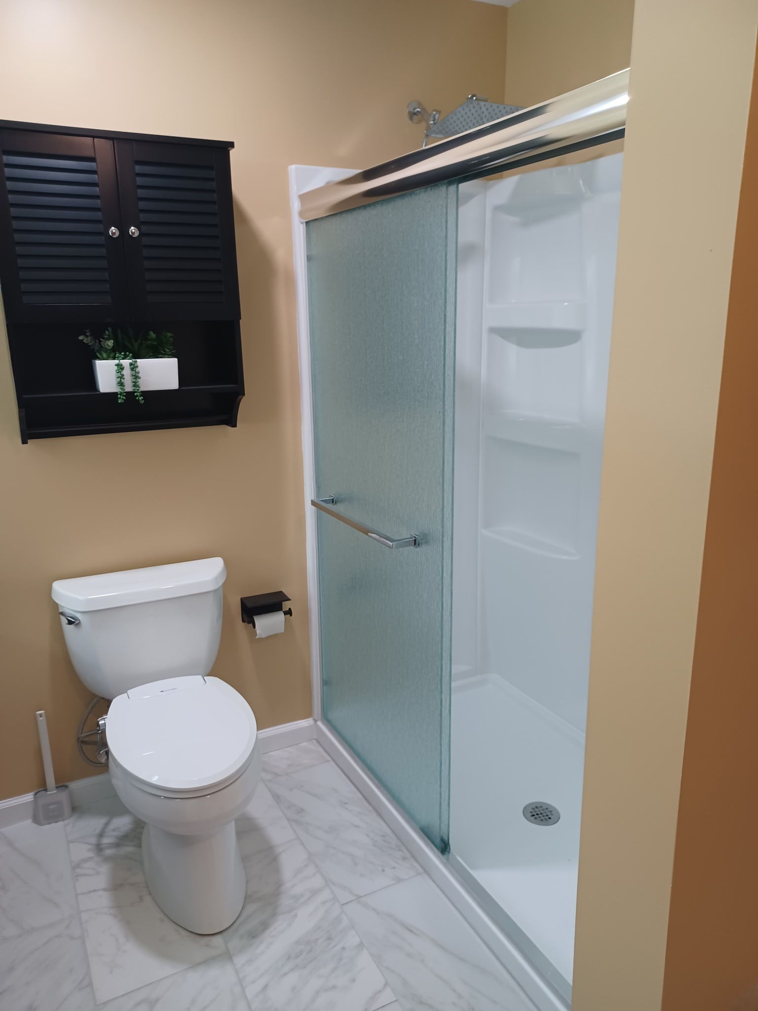 Bathroom with a white toilet, shower with glass door, and a black cabinet.