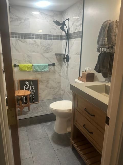Bathroom with walk-in shower, toilet, and vanity with concrete countertop. Gray and white tile, wooden vanity.