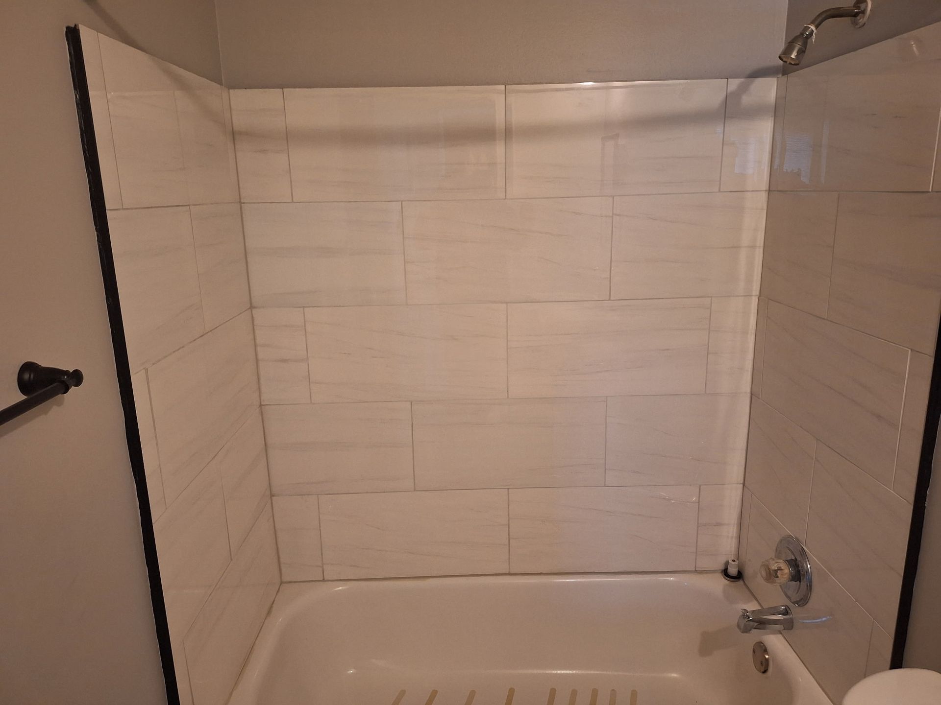 White-tiled shower stall with a curved shower rod over a bathtub. Black trim lines the shower walls.