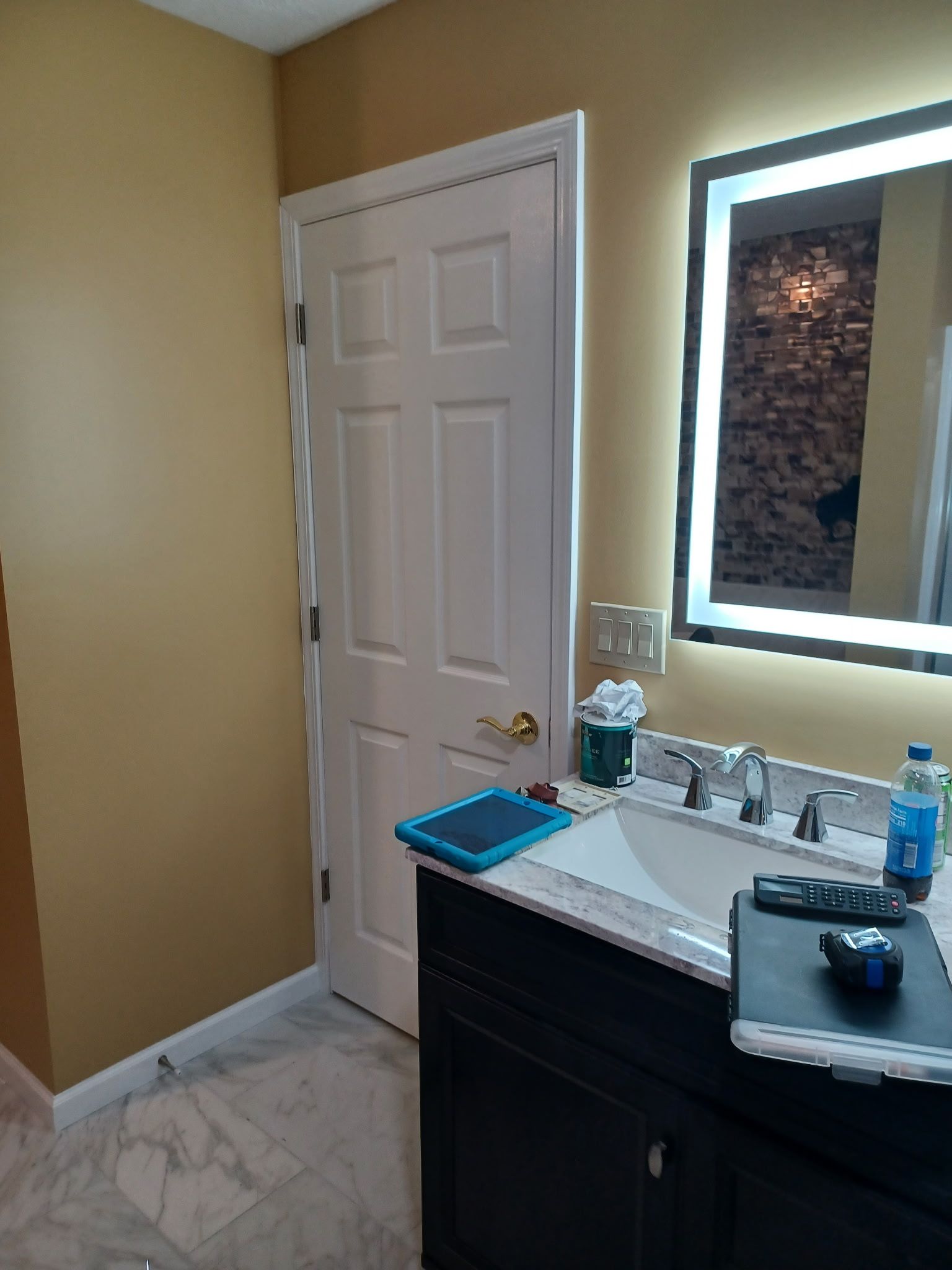 Bathroom with black vanity, white sink, backlit mirror, door, and tan walls.