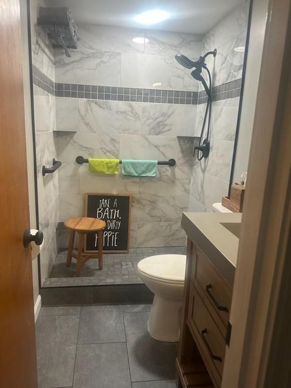 A modern bathroom with a walk-in shower. Gray tile, marble-look shower walls, and a wooden vanity.