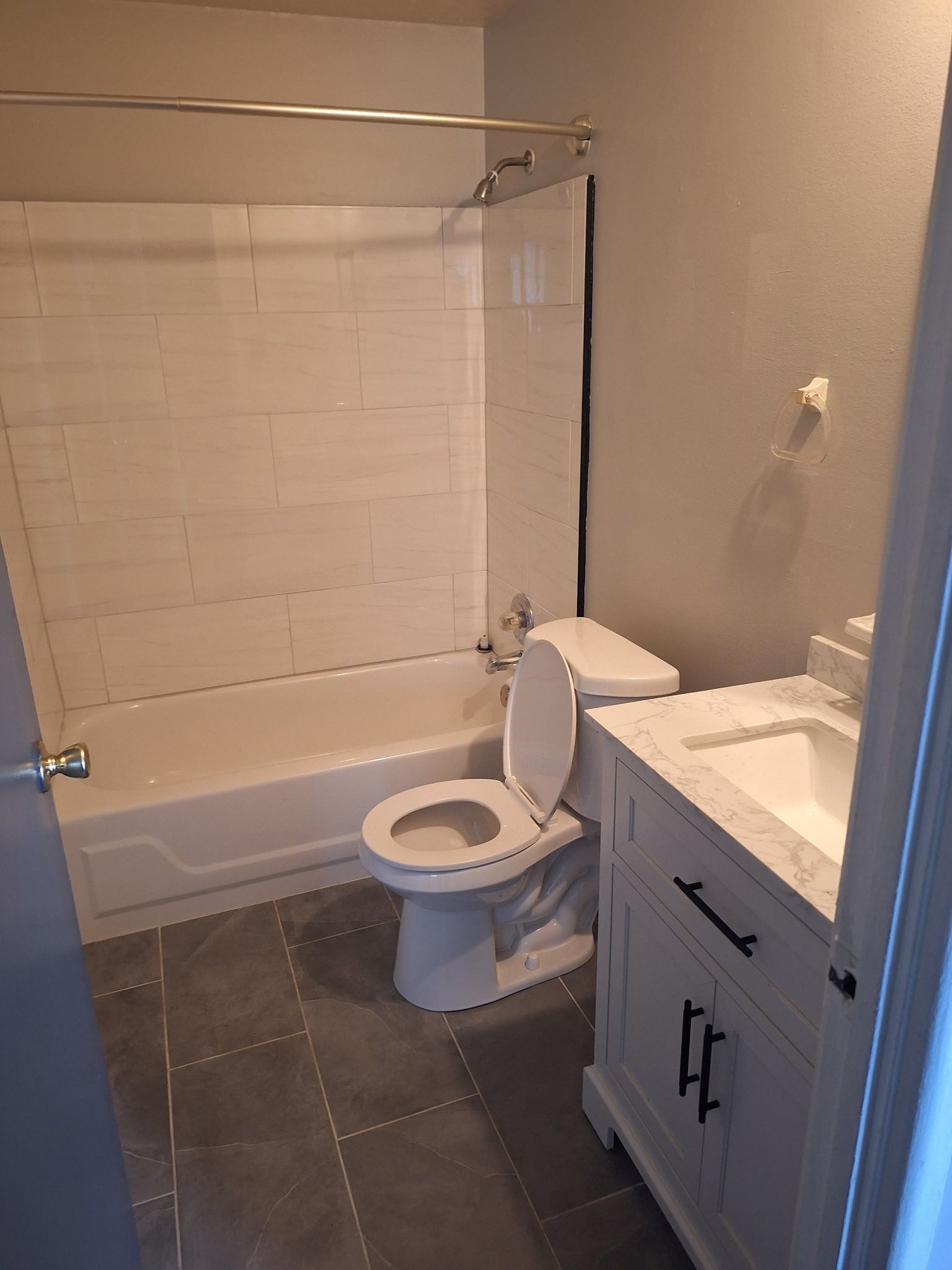 Bathroom with white tub/shower, toilet, vanity, and gray tile floor.