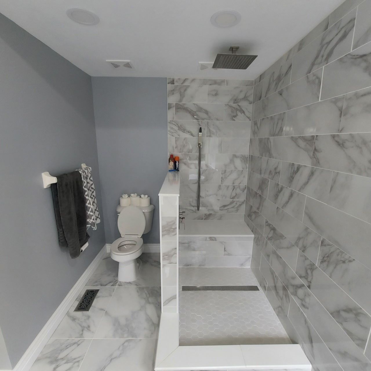 Bathroom with gray walls and marble-tiled shower. Toilet, towel rack, and shower bench visible.