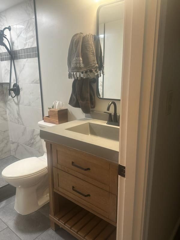 Bathroom with toilet, wooden vanity, shower, and mirror; towels hanging.