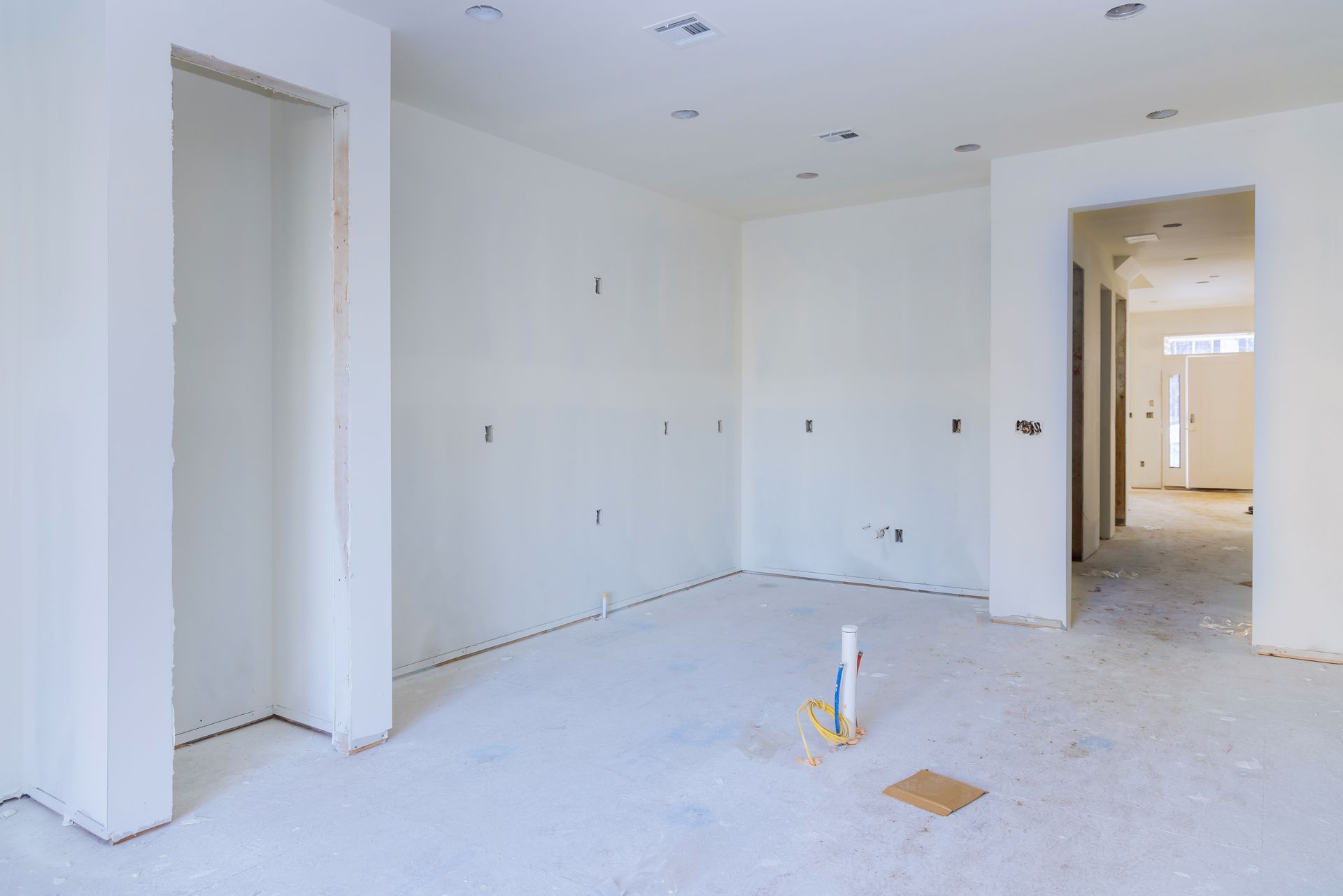 Interior of a room under construction, white walls, exposed wiring, open doorways, unfinished floor.