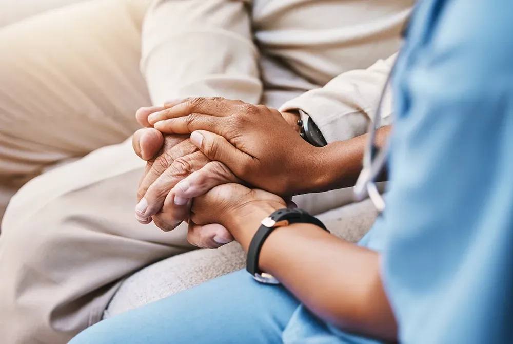 A person's hands are clasped by a person wearing a blue medical uniform, offering comfort.