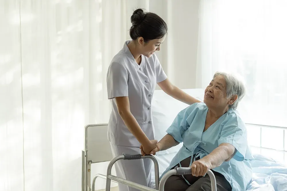 Nurse assisting patient with a walker in a hospital room.