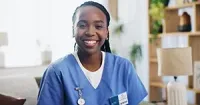 Smiling healthcare worker wearing blue scrubs in a home setting.