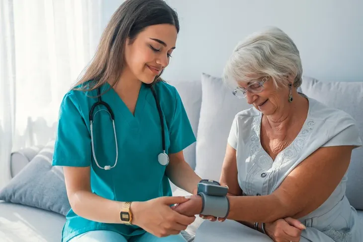 A healthcare worker in scrubs taking an older adult's blood pressure with a cuff on their wrist.