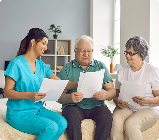 Nurse in blue scrubs reviews paperwork with two older adults indoors.