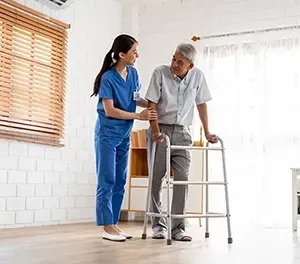 Caregiver assisting a person using a walker in a room with a window.