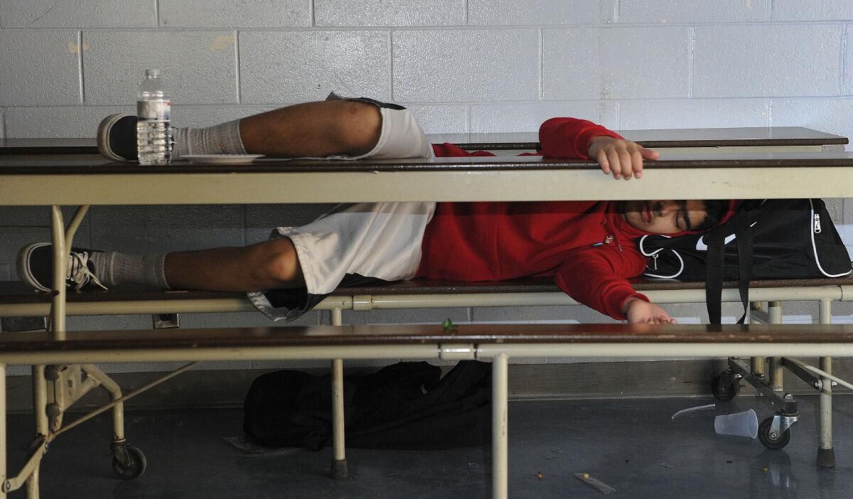 A person in a red hoodie is laying under a table A person in a red hoodie is laying under a table