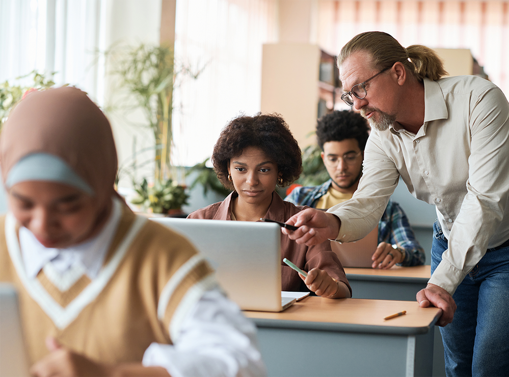 A man is teaching a group of students how to use a laptop computer in a classroom.