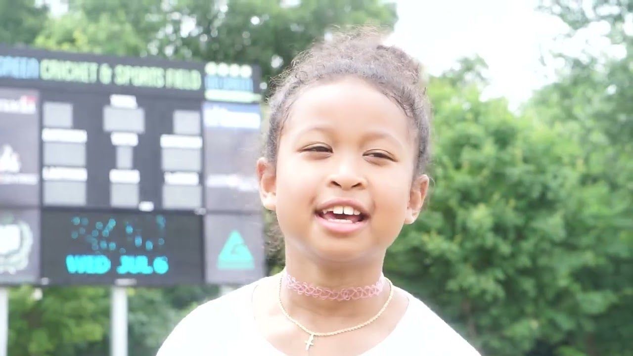 A little girl is standing in front of a scoreboard.