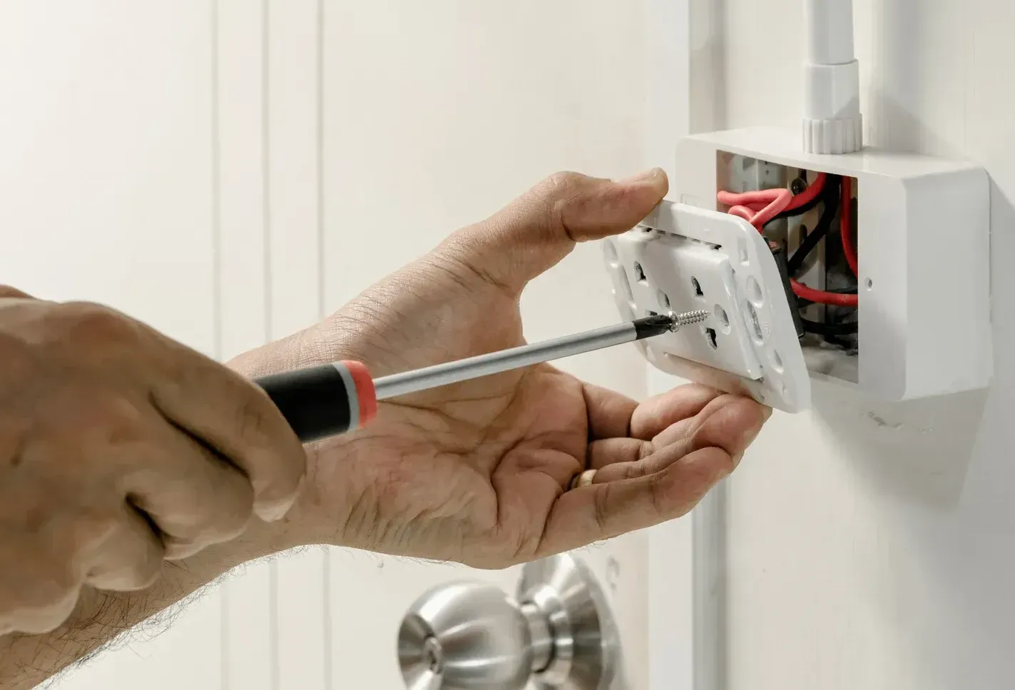 A man is fixing an electrical outlet with a screwdriver.