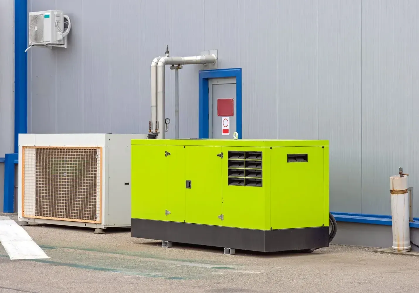 A green generator is parked in front of a building.
