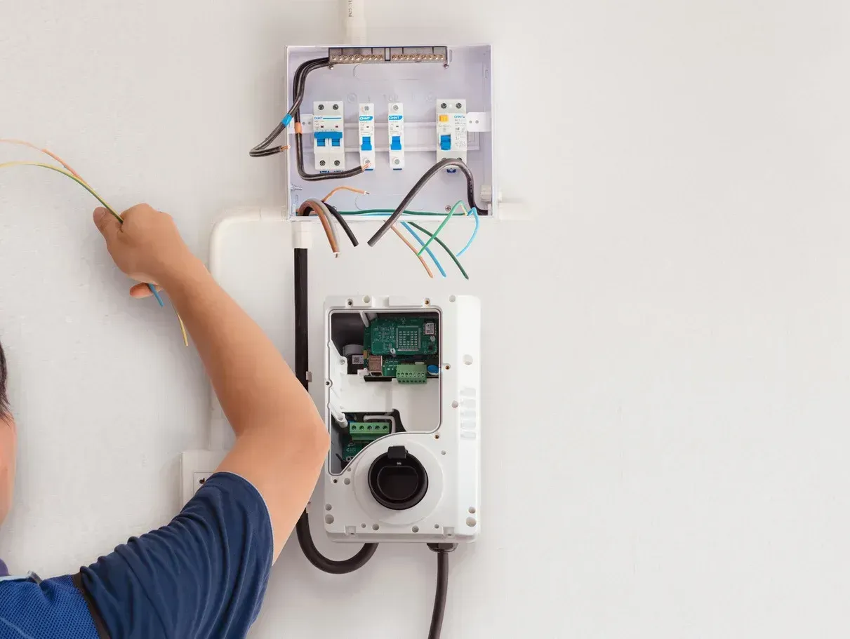 A man is working on an electrical box on a wall.