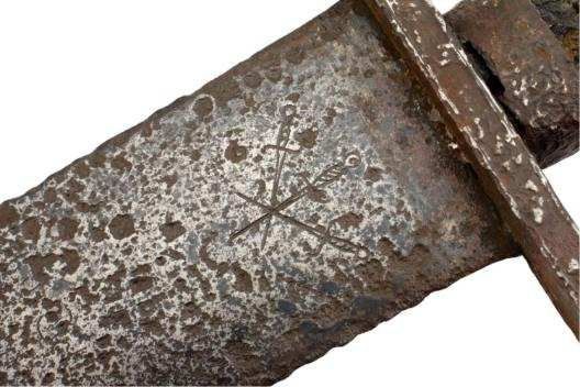 Close-up of a rusty sword blade with an etched emblem featuring a sword crossed with two arrows.