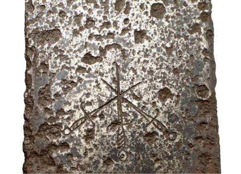 Close-up of weathered, metal surface with etched design of three crossed swords.