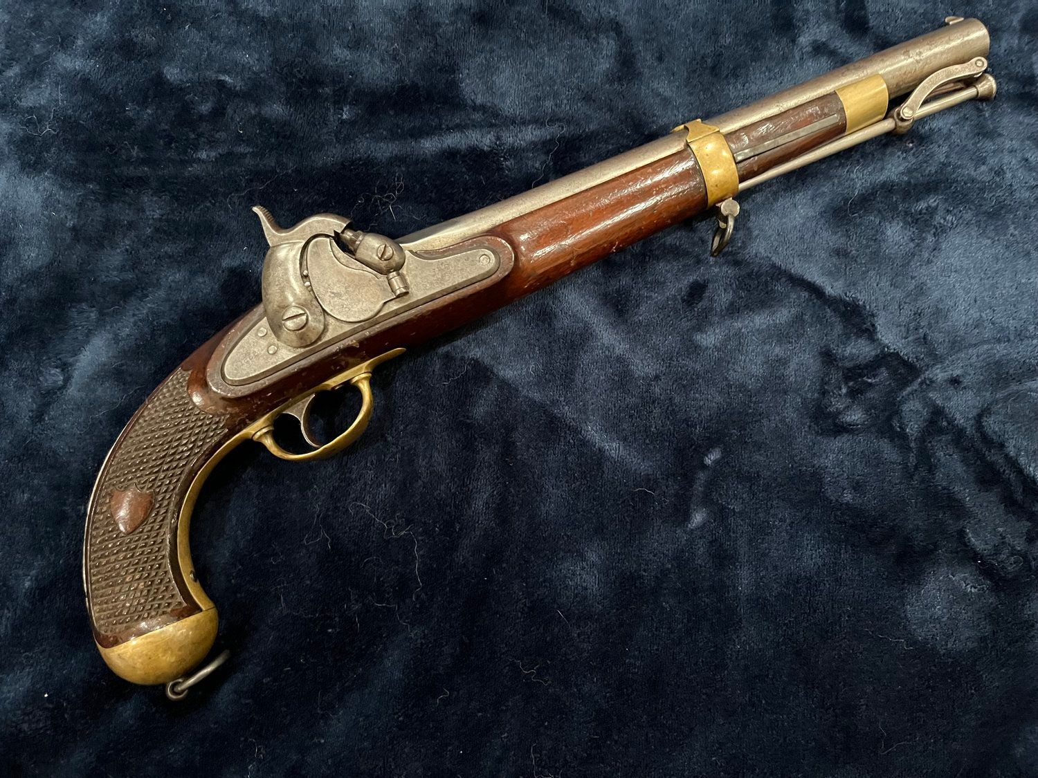 Antique pistol with a wooden handle and silver and gold metal accents, resting on a dark blue velvet surface.