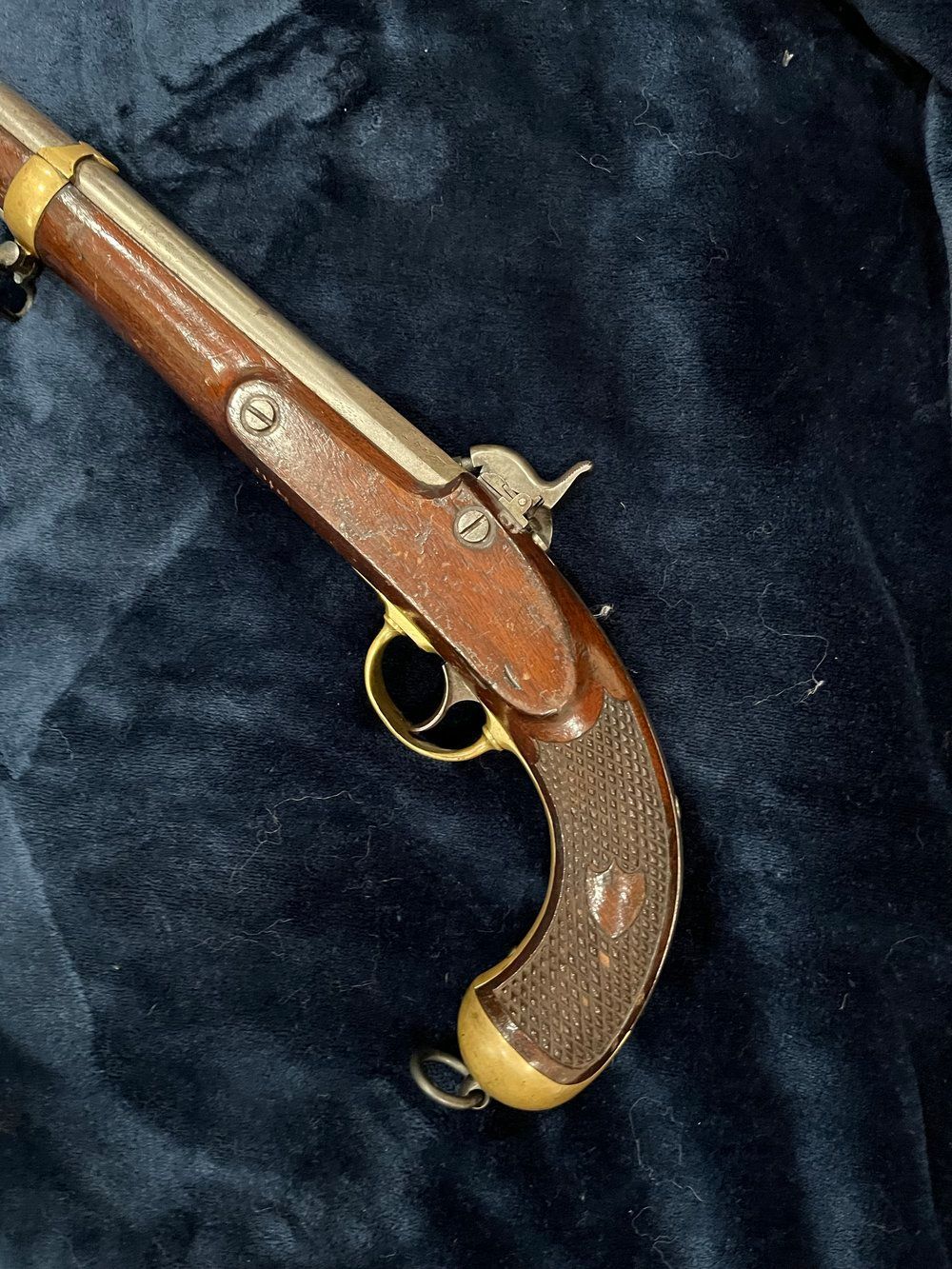 Antique pistol with a wooden handle and silver and gold metal accents, resting on a dark blue velvet surface.