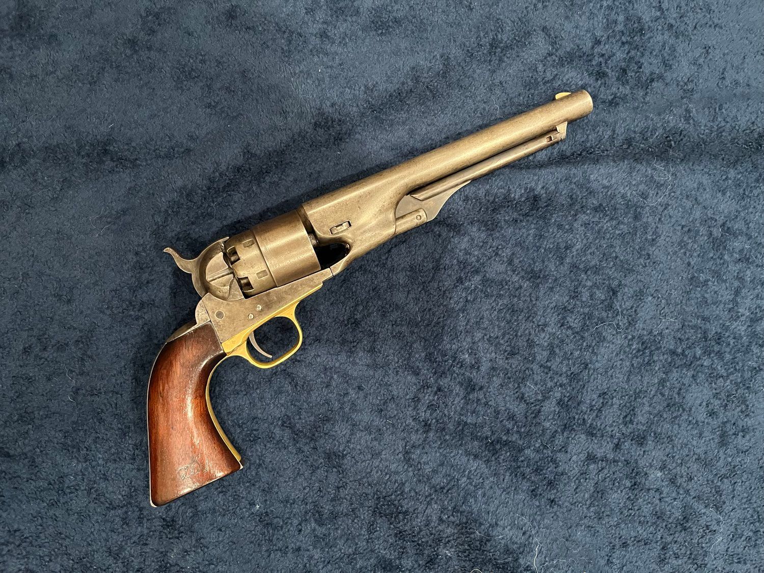 A brass revolver with a wooden handle is sitting on a blue cloth.