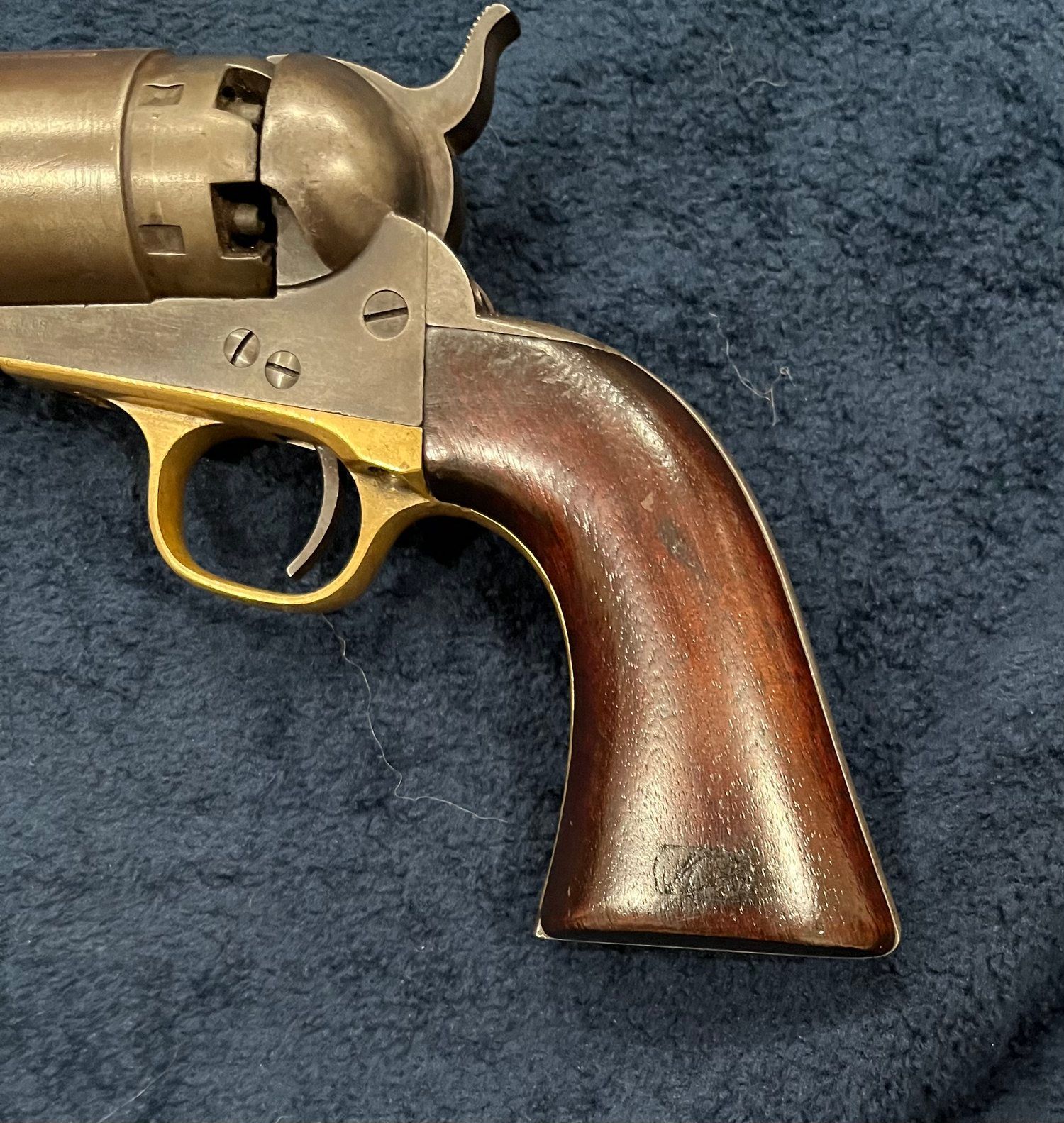 A brass revolver with a wooden handle is sitting on a blue cloth.