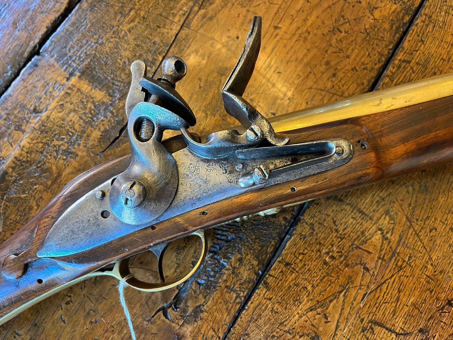 A long, antique flintlock rifle with a wooden stock and brass accents rests on a hardwood floor.