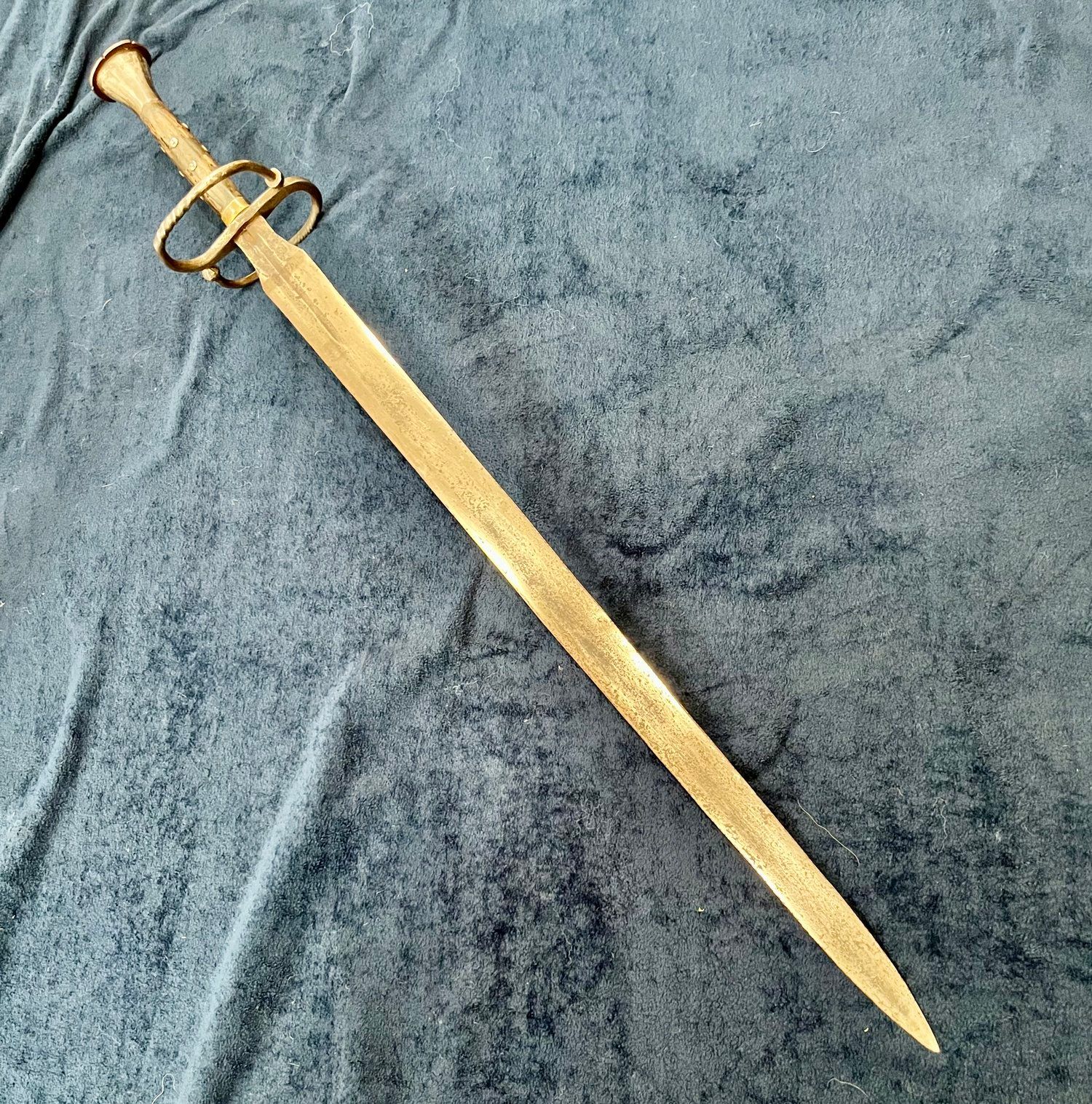 A long, antique sword with a cross-guard ring on a wrinkled, blue fabric surface.