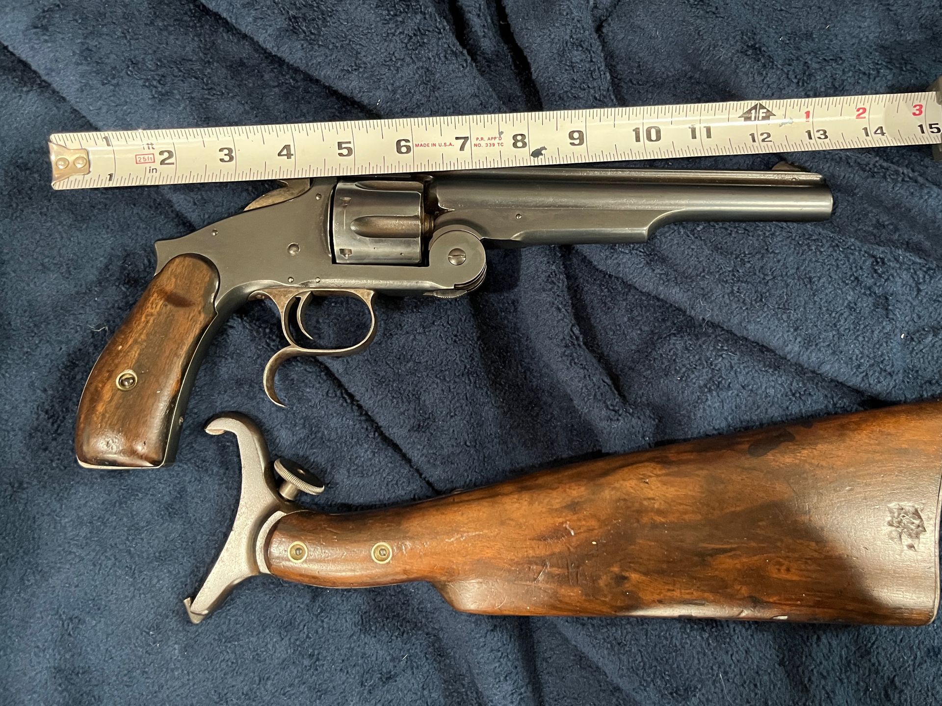 Antique revolver with wooden shoulder stock on a dark blue fabric.