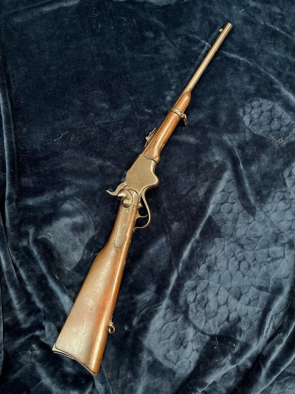Antique lever-action rifle with wooden stock and brass accents, lying on a dark blue textured surface.