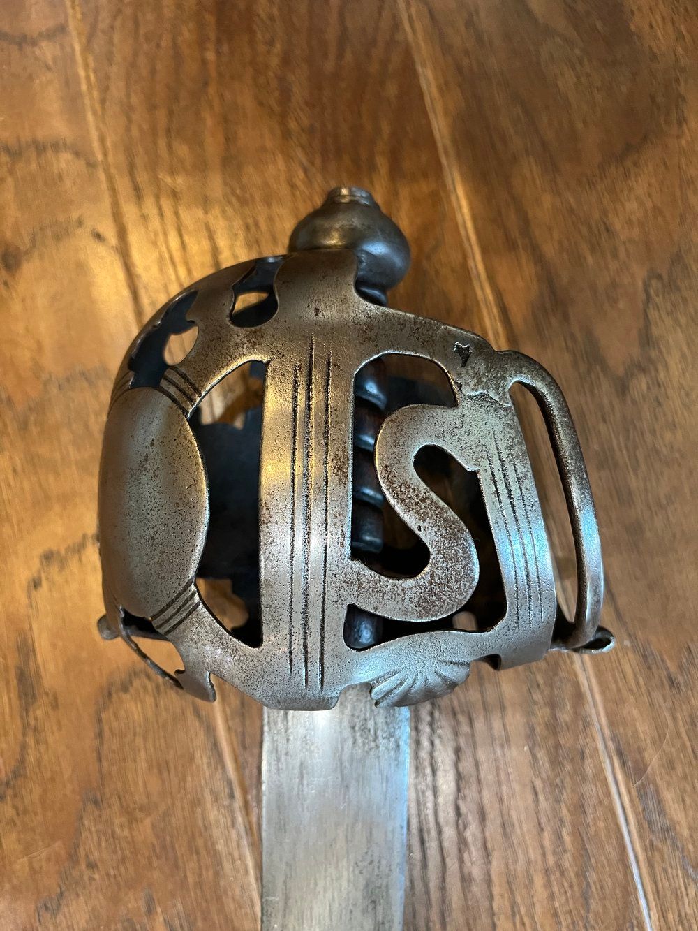 Close-up of a sword hilt with a decorative, openwork guard featuring the initials "IS".