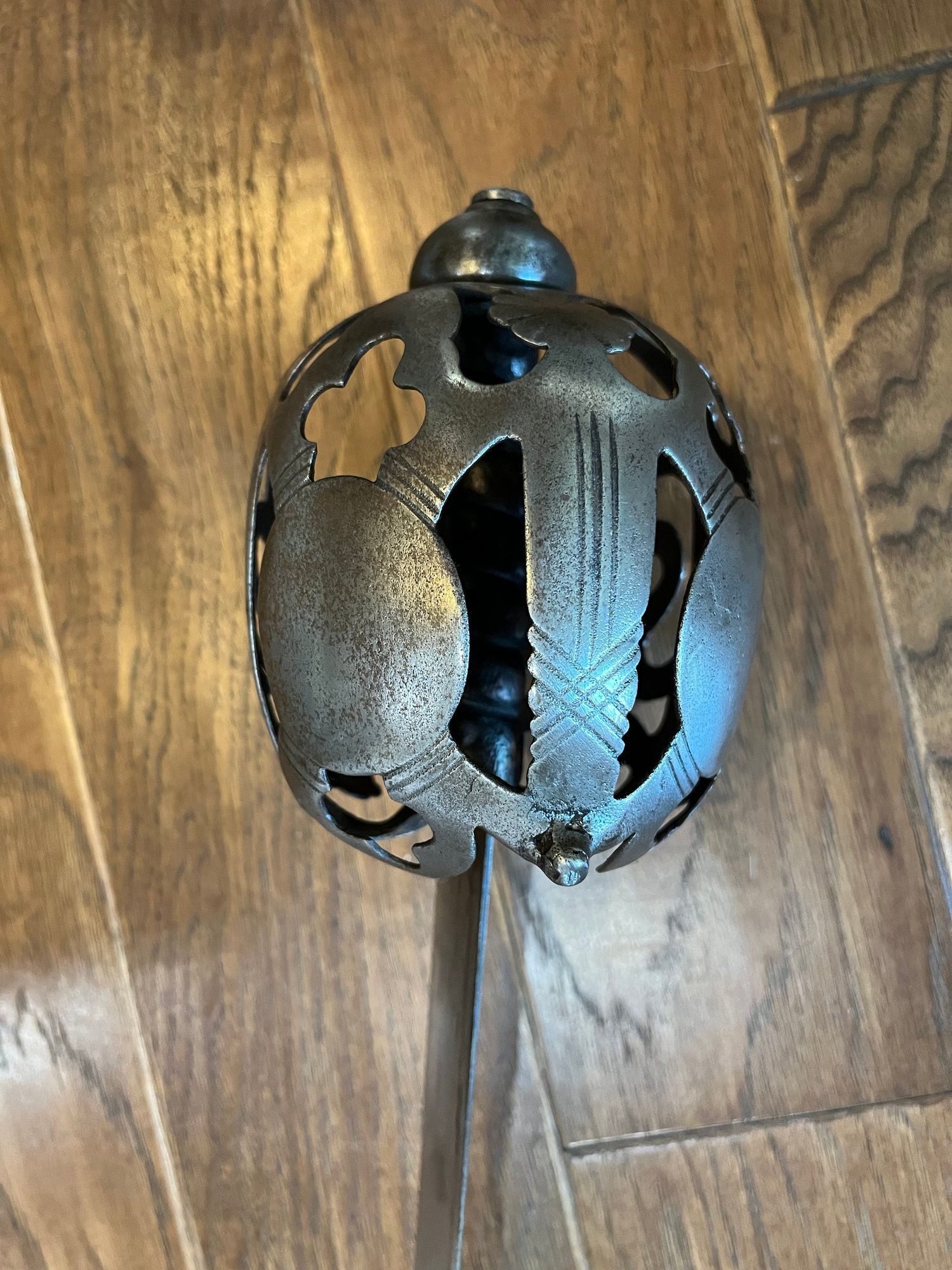 Close-up of a sword hilt with a decorative, openwork guard featuring the initials 